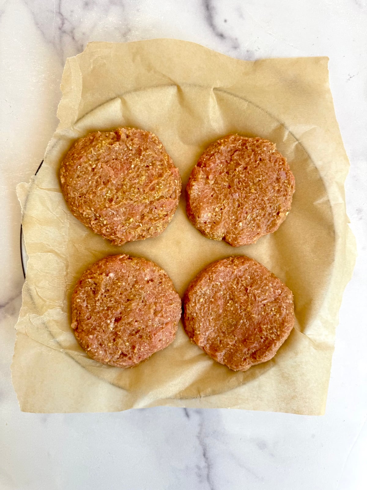 Four raw turkey burger patties formed and placed on parchment paper ready to cook.