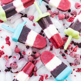 Homemade red, white and blue popsicles with layers of raspberry, creamy yogurt, and blueberry, resting on ice with fresh berries.