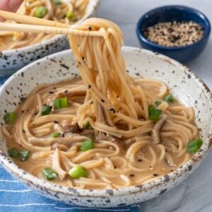 Person's hand using chopsticks to grab ramen noodles from bowl of ramen noodle soup.