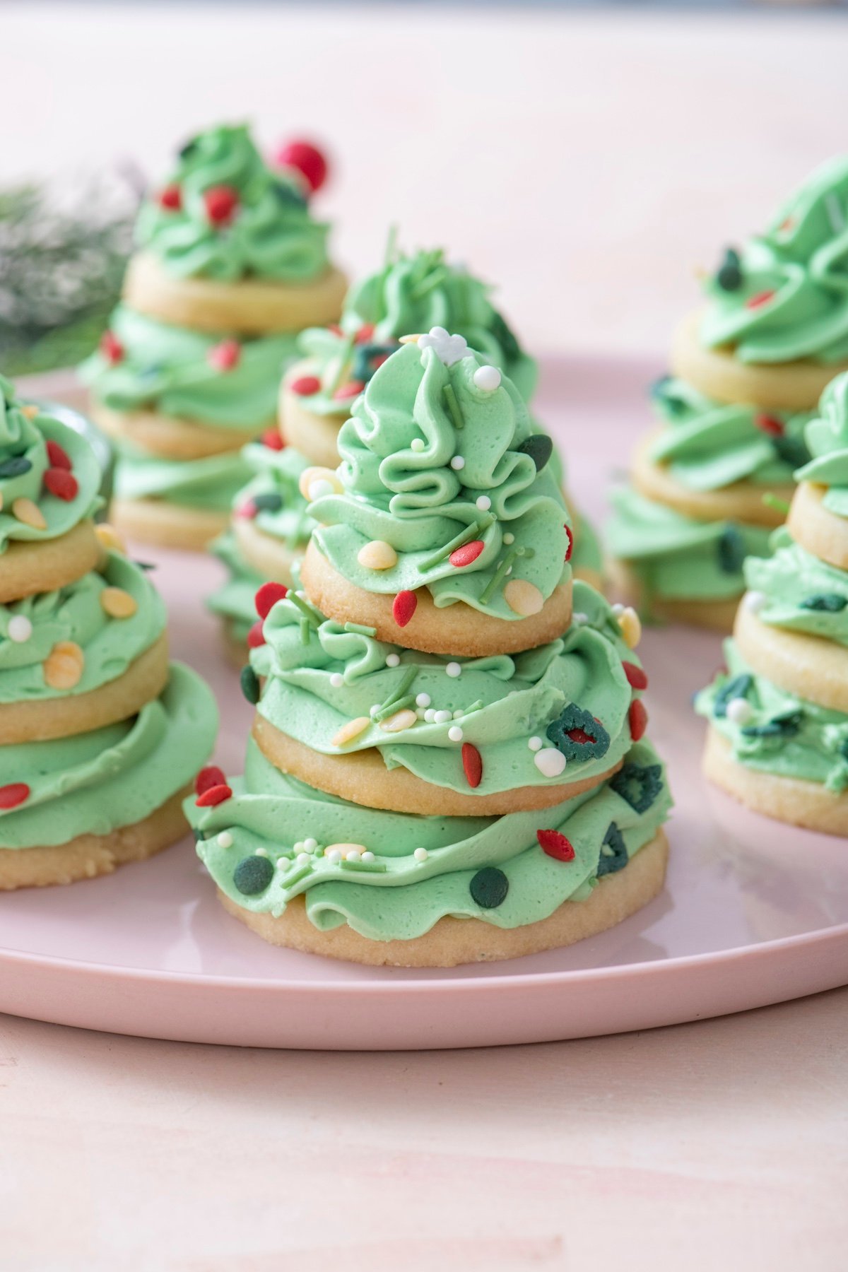 Sugar cookies stacked with swirls of green buttercream to create a Christmas tree shape. Topped with sprinkles.