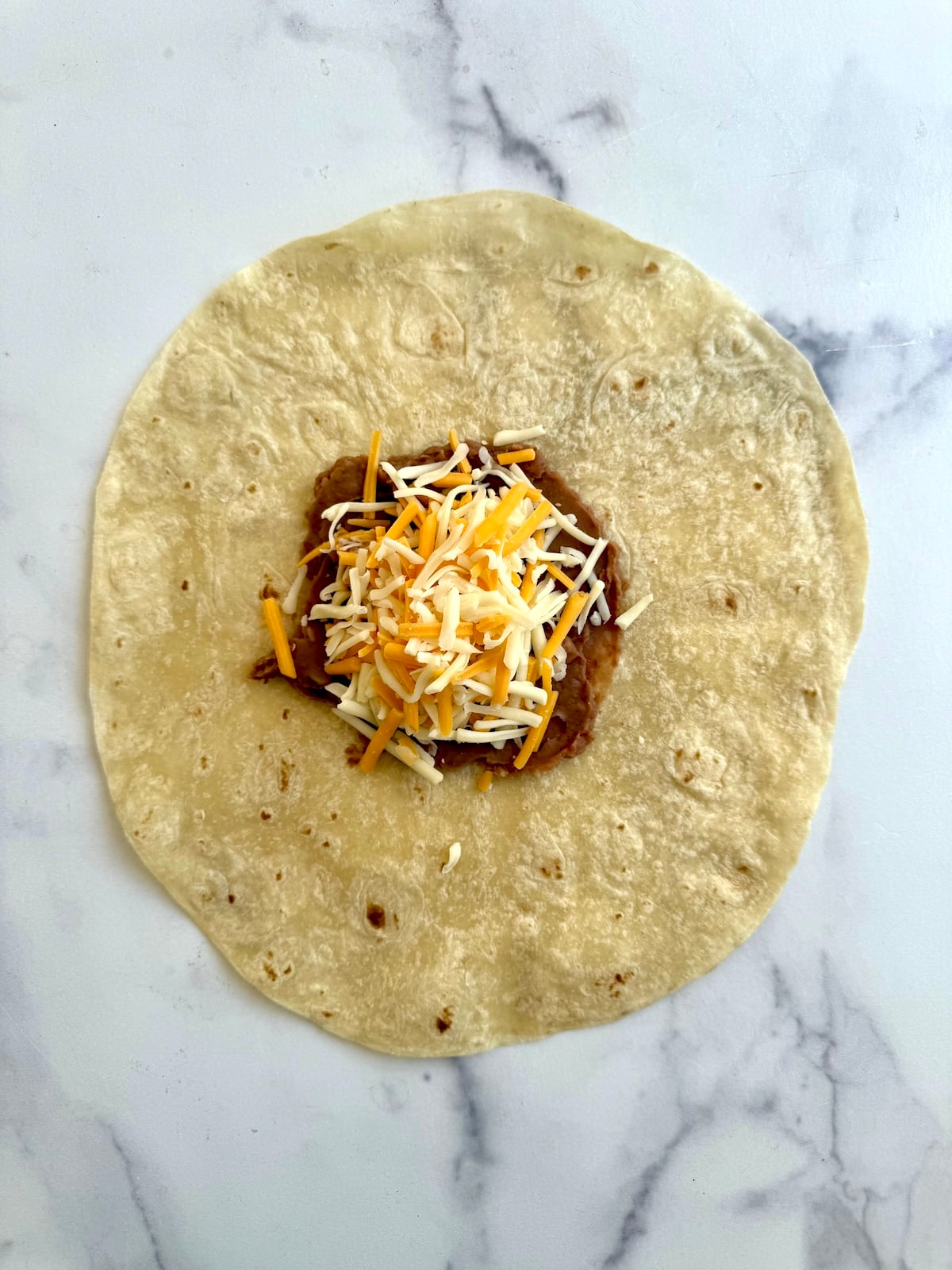 Refried beans and shredded cheese on top of a tortilla.