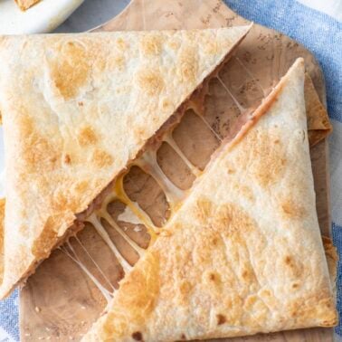 Air fryer tortilla pillow cut in half on a cutting board.