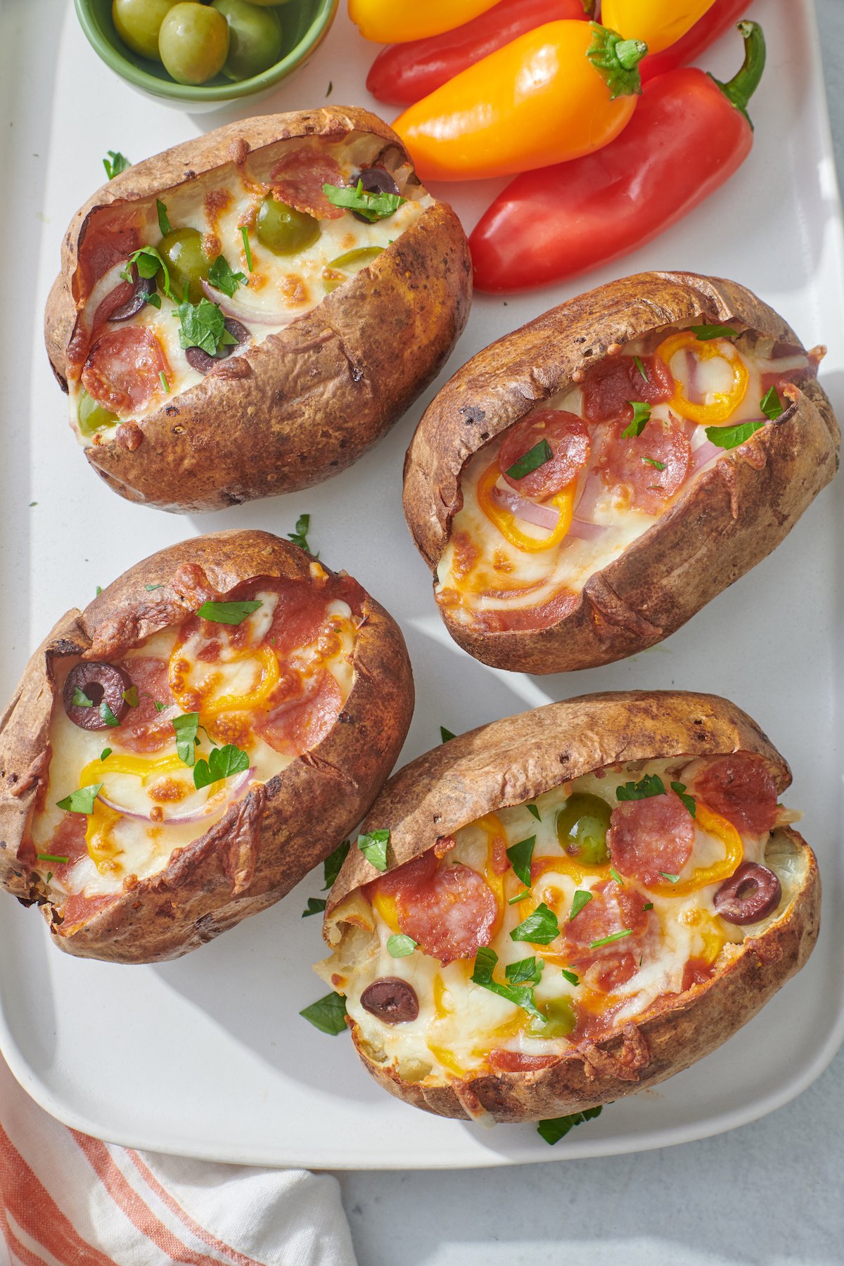 four pizza stuffed potatoes on a platter with mini peppers