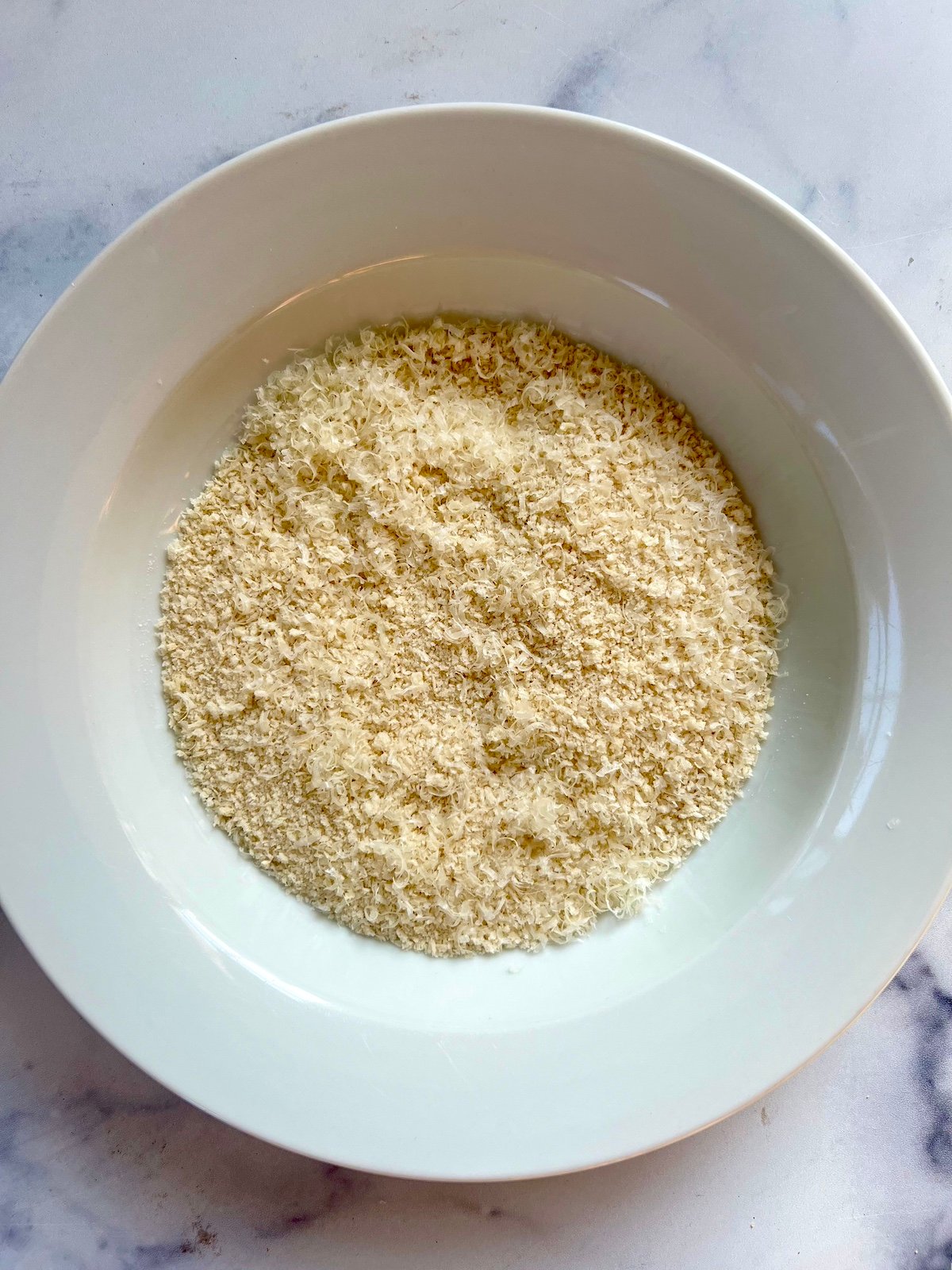 Breadcrumbs and parmesan cheese combined in shallow bowl.