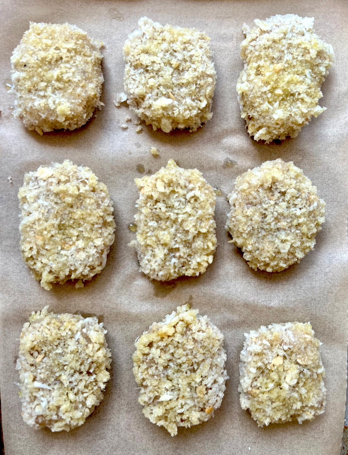 Breaded chicken nuggets on baking sheet lined with parchment paper.