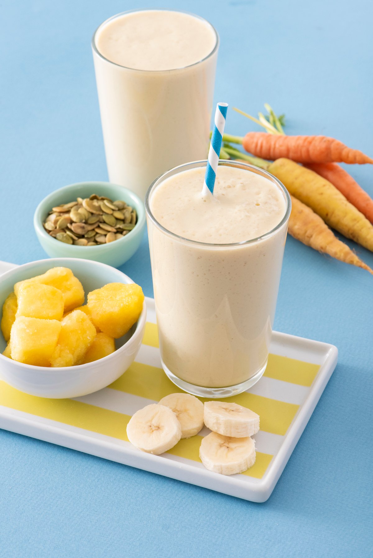 PMS Smoothies with pineapple, pumpkin seeds and carrots around them.