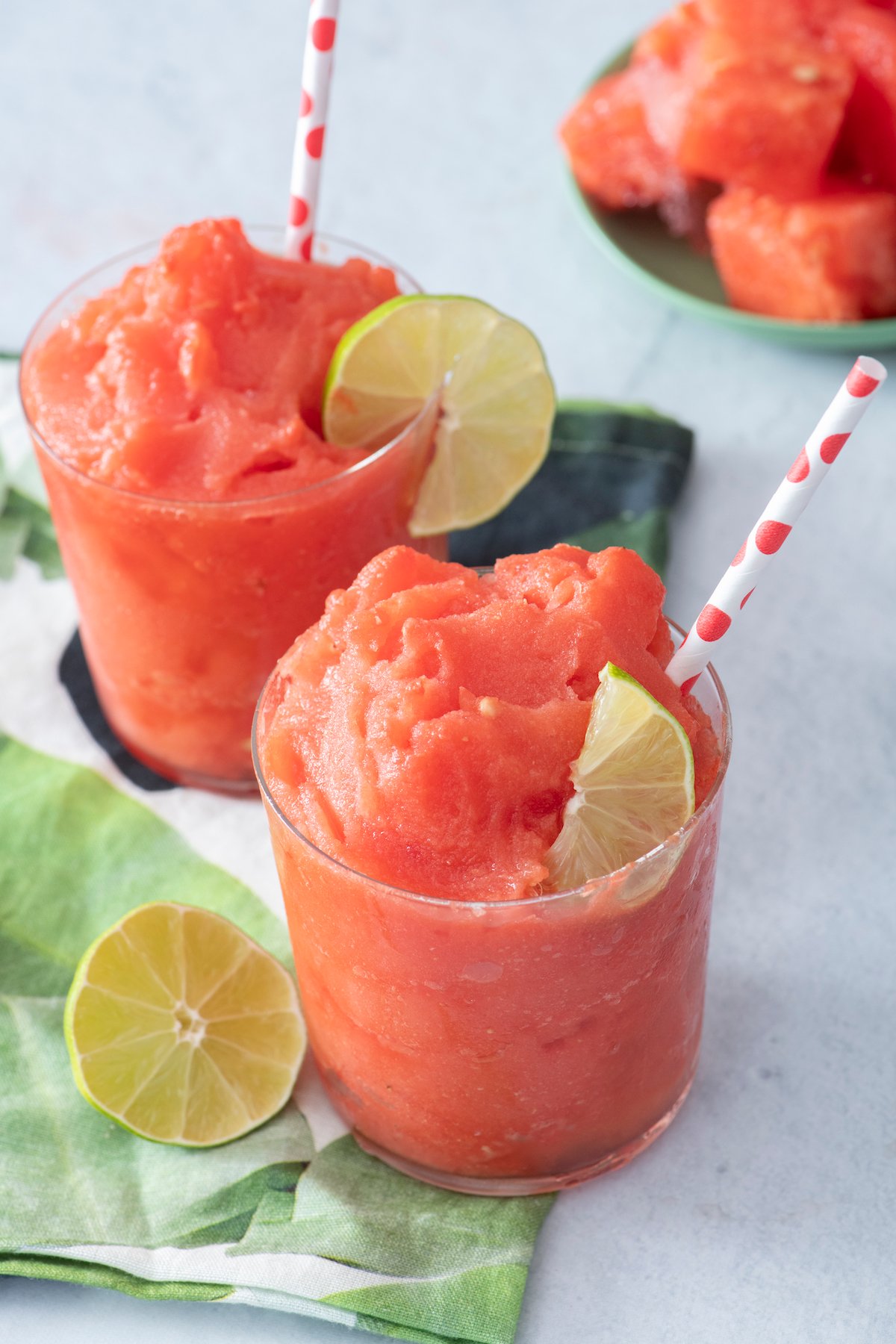 Two watermelon slushies in clear glasses served with lime wedges.