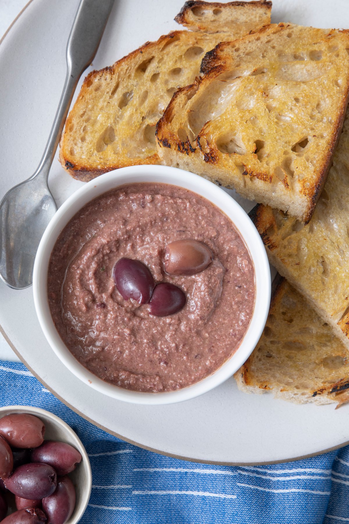 Olive tapenade in small bowl with crispy bread on the side.