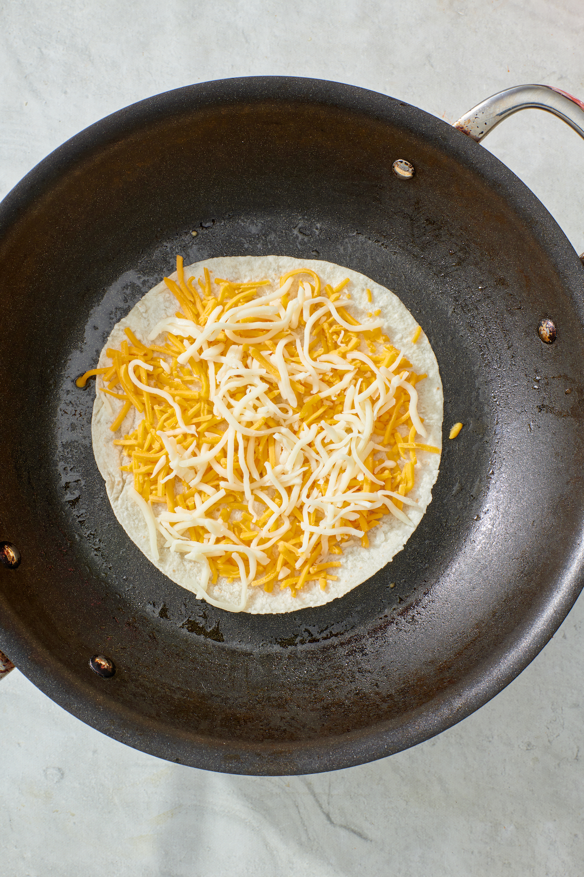 Cheese on tortilla in frying pan.
