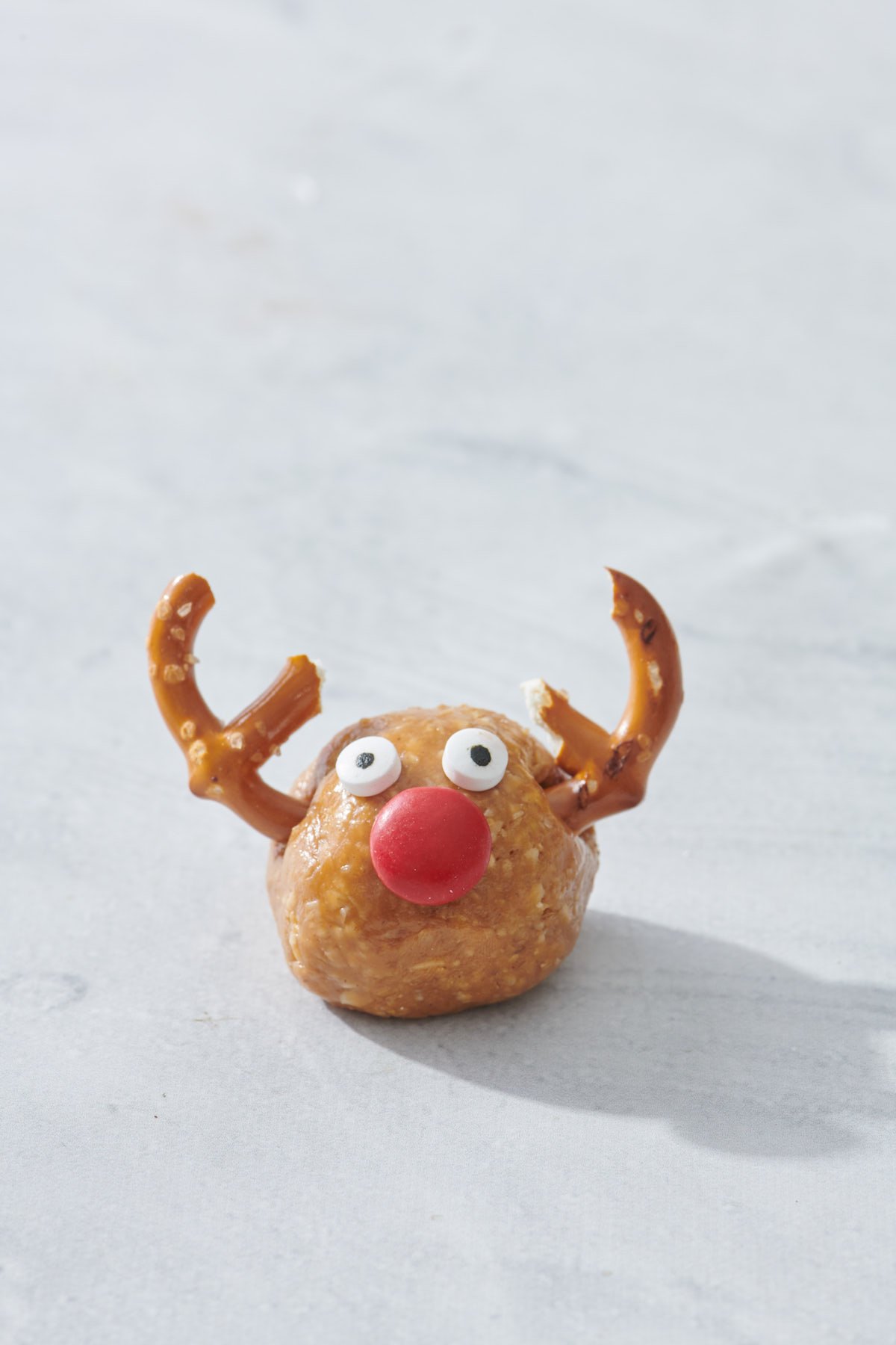 peanut butter oatmeal ball with pretzel antlers, red candy nose and candy eyes to form No-Bake Reindeer Bite