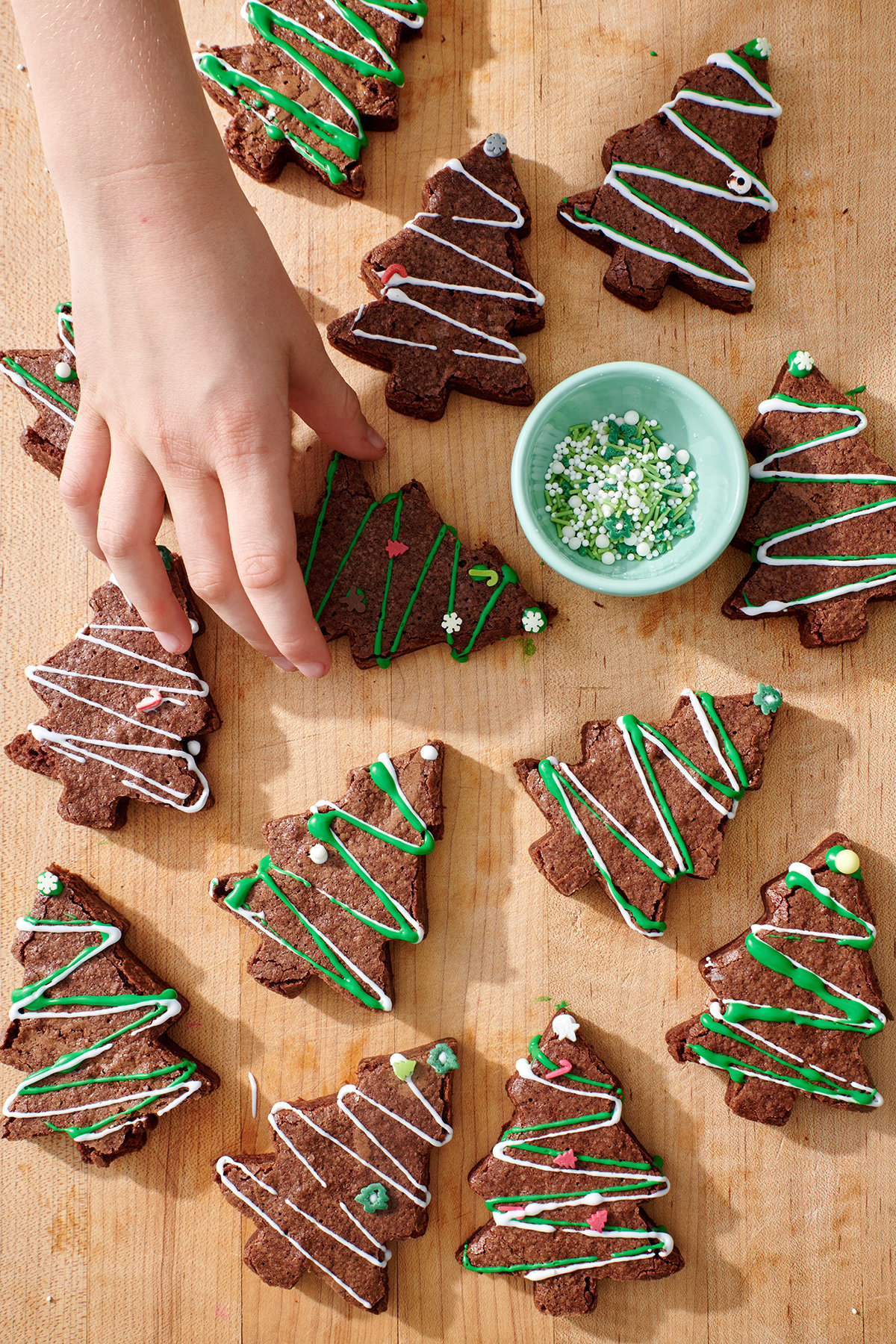 Child's hand grabbing Christmas tree brownie off of serving board.