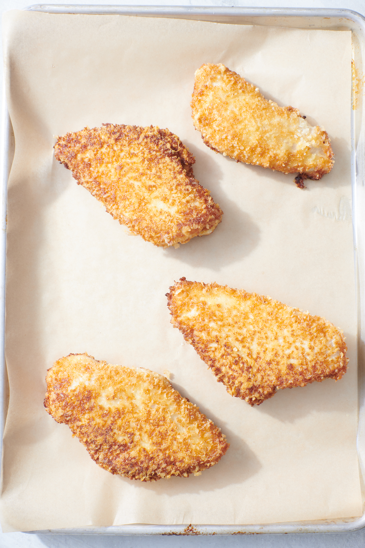 Breaded chicken on parchment paper lined baking sheet.