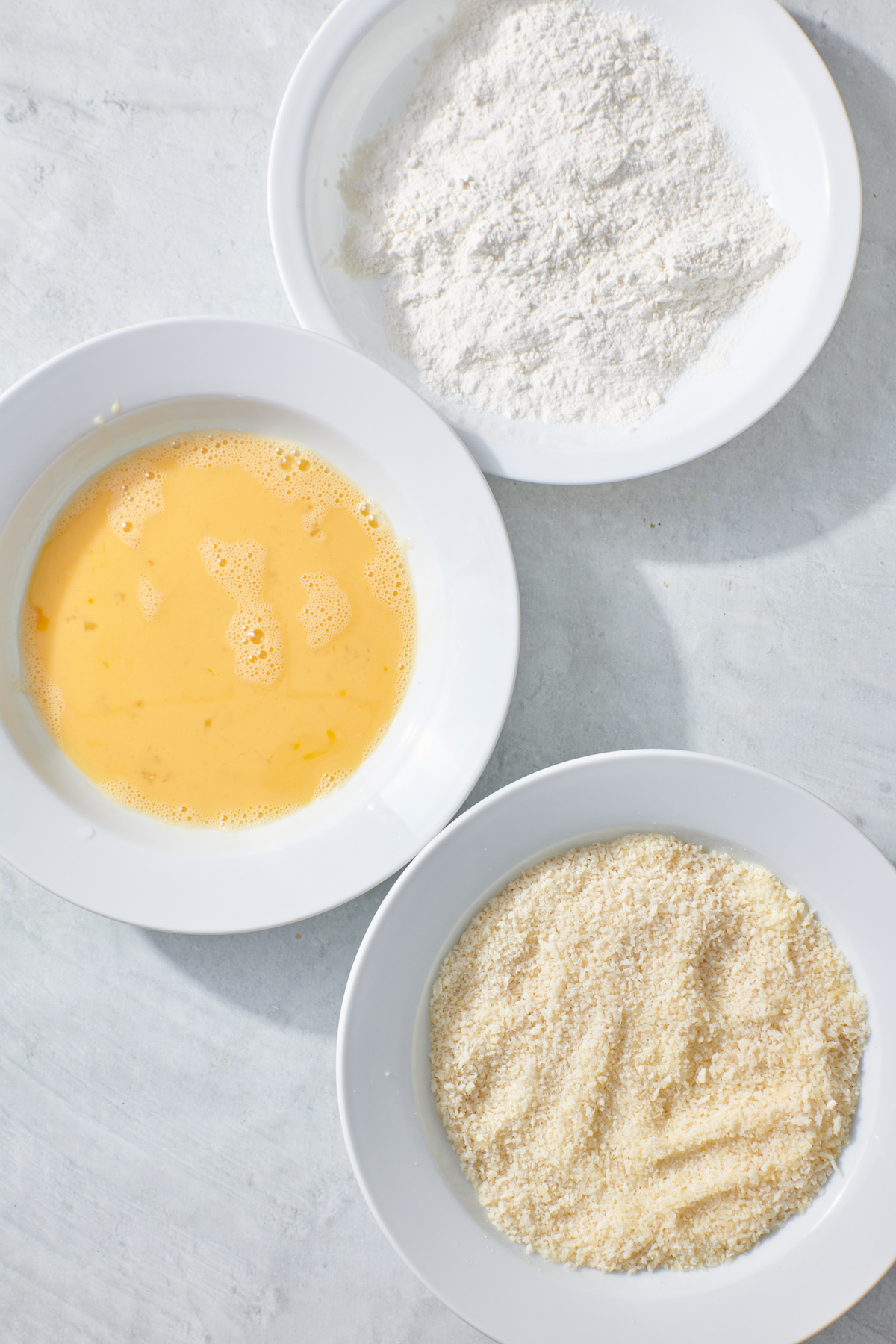 Breading station: flour in a bowl, whisked eggs in a second bowl, panko in a third bowl.