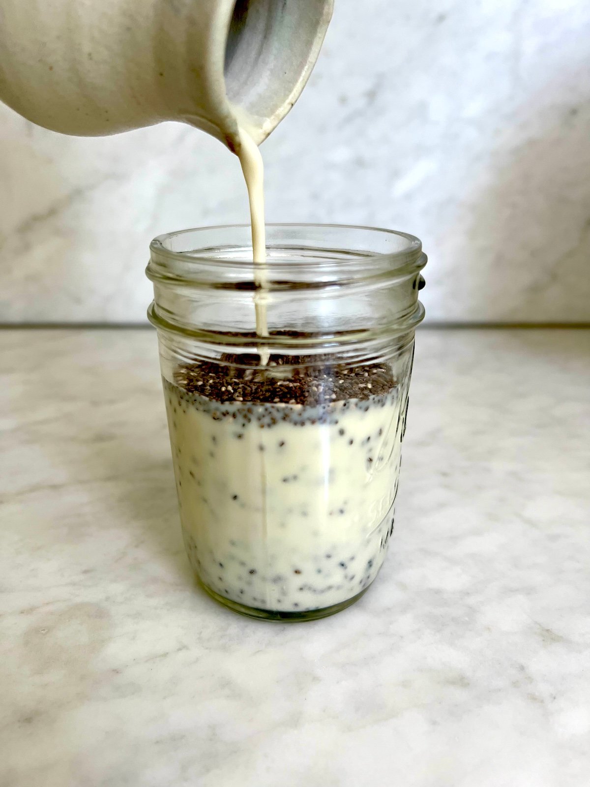 Pouring milk into mason jar with chia seeds.