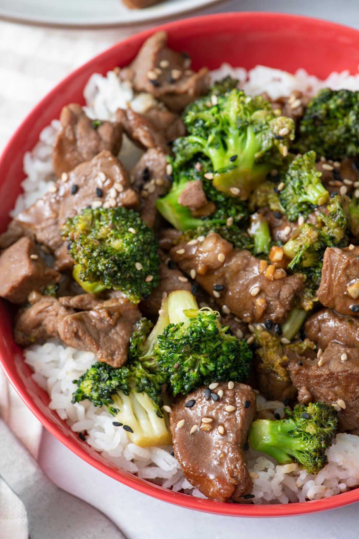 Beef and broccoli served over white rice in red bowl.