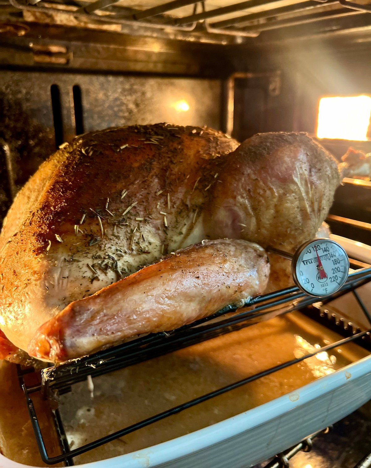 Herb brined turkey in oven with meat thermometer inserted in thigh.