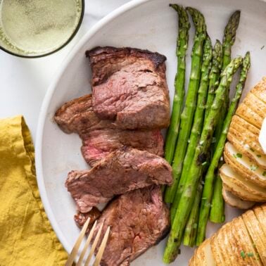 Sliced beef tenderloin on plate with asparagus and baked potato.