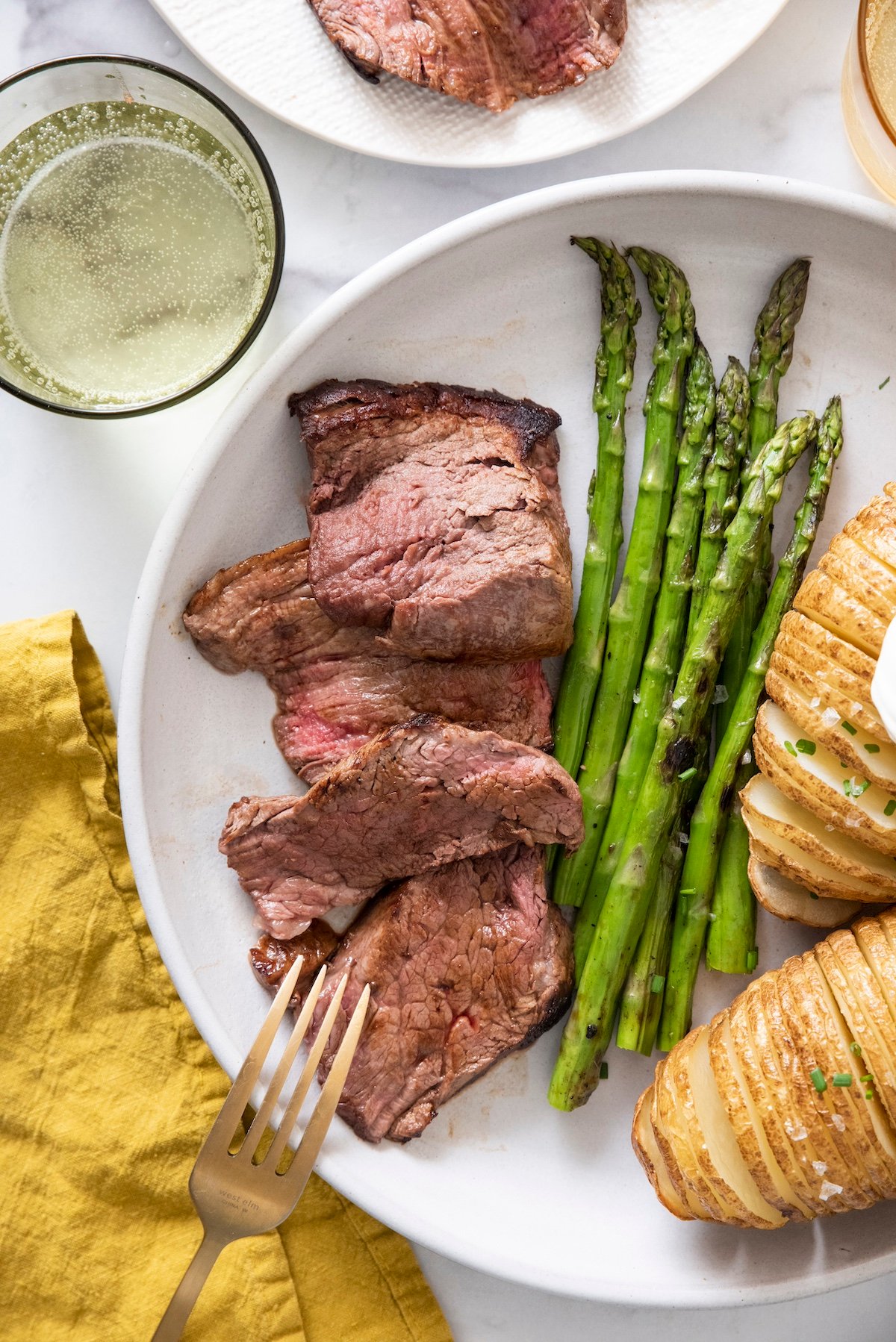 Sliced beef tenderloin on plate with asparagus and baked potato.