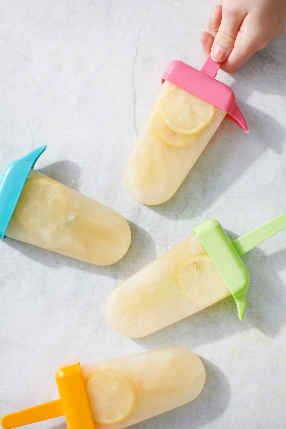 Hand grabbing Wellness Electrolyte Popsicle from marble surface.