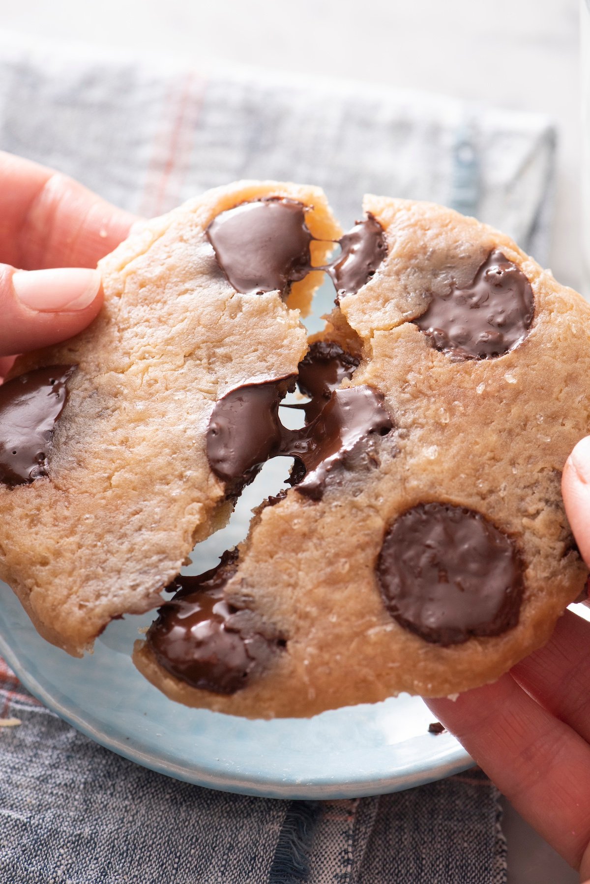 Hands breaking a microwave chocolate chip cookie in half.