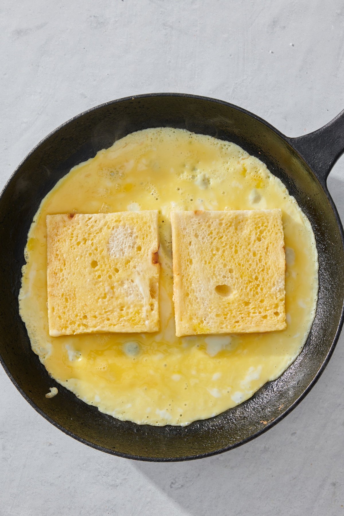 Two slices of bread on top of eggs in a skillet.