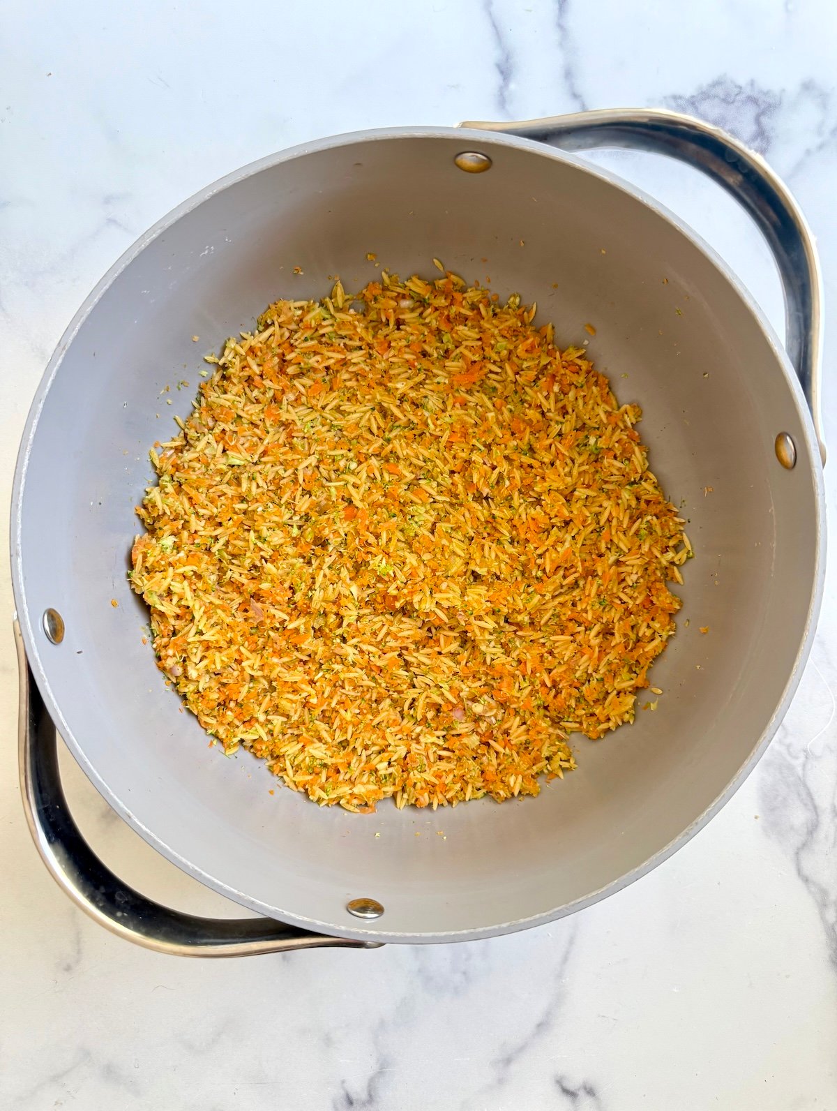 Sauteed carrots, broccoli and orzo in a stock pot.