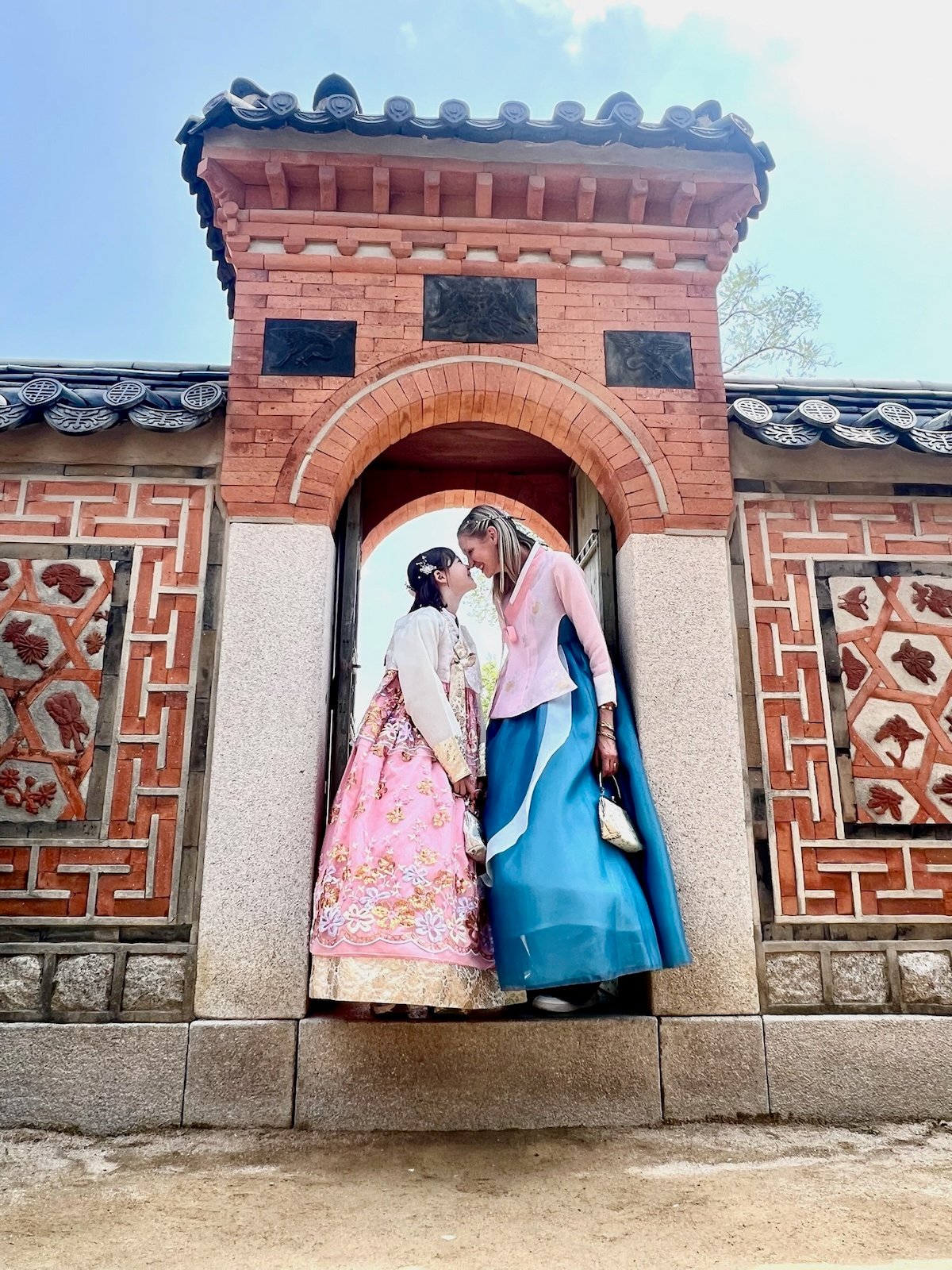 Mother and daughter dressed in traditional hanbok dresses in a doorway.