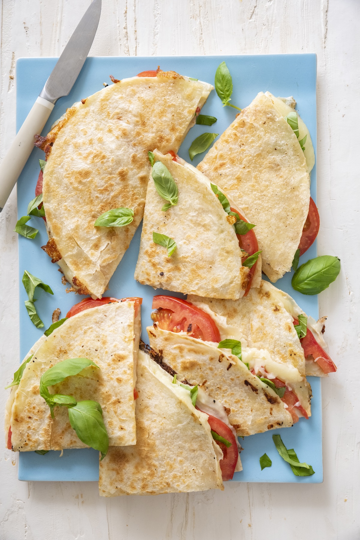 Caprese quesadillas on blue cutting board.