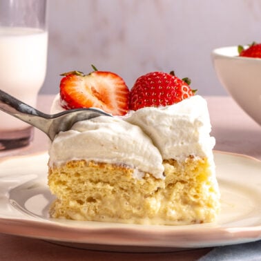A fork scooping a bite from a piece of tres leches cake.