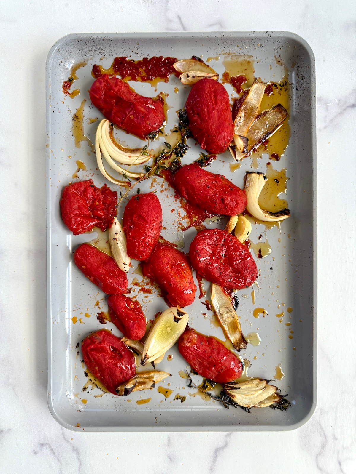 Roasted tomatoes, onions and thyme on a sheet tray.
