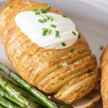 Hassleback potato on a plate topped with sour cream and chives.