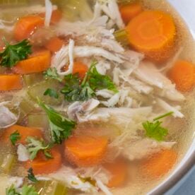 A bowl of pressure cooker chicken soup with carrots and topped with parsley.