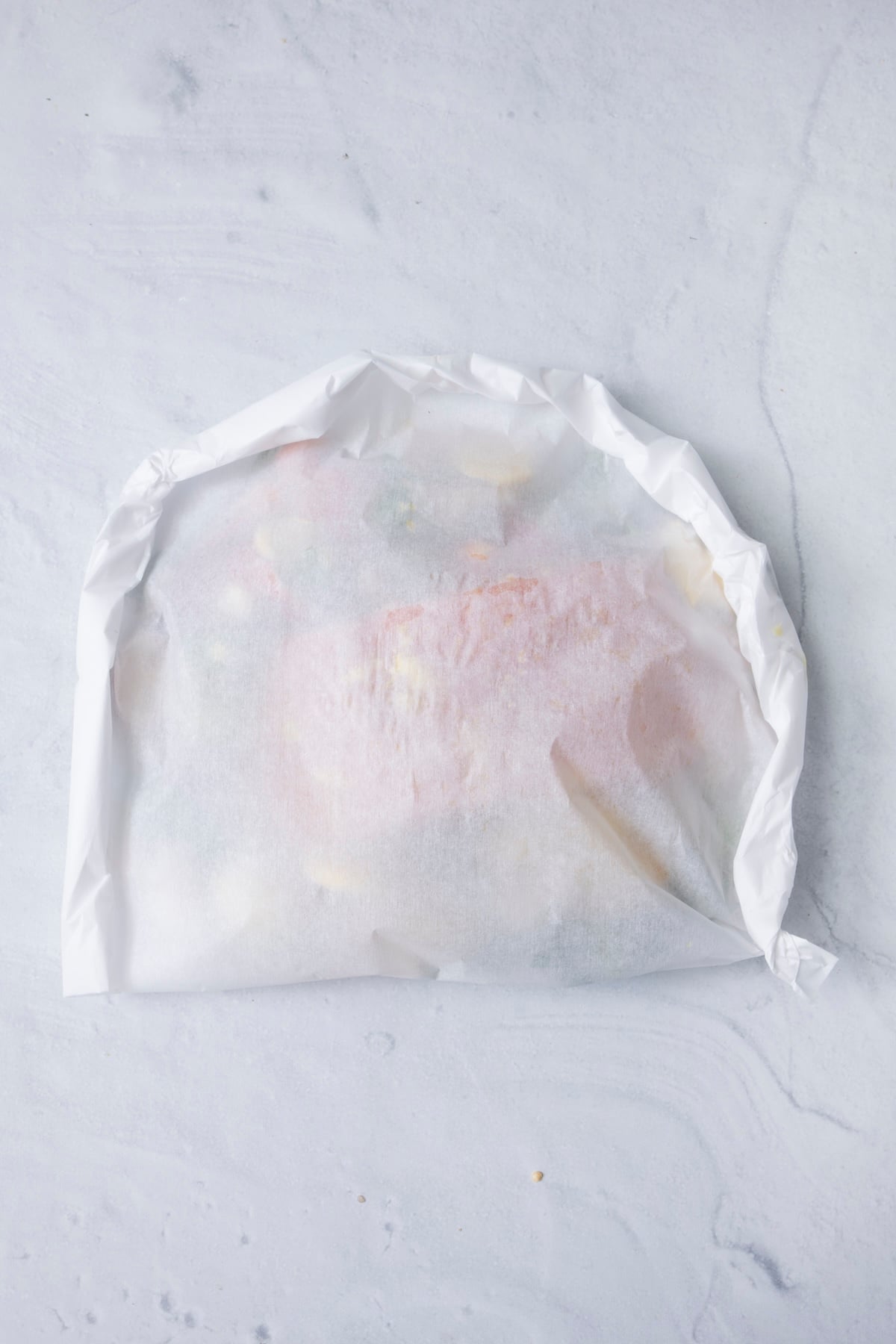 A single sealed fish en papillote packet on a white marble surface, ready to bake.