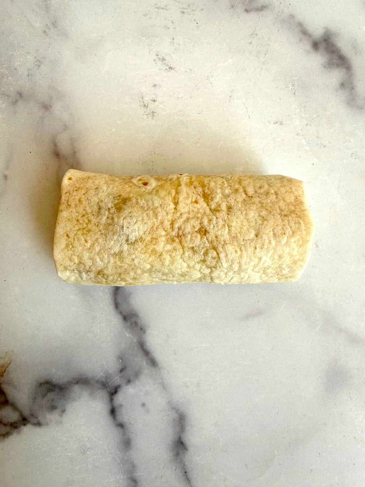A rolled up burrito ready to toast in a skillet.