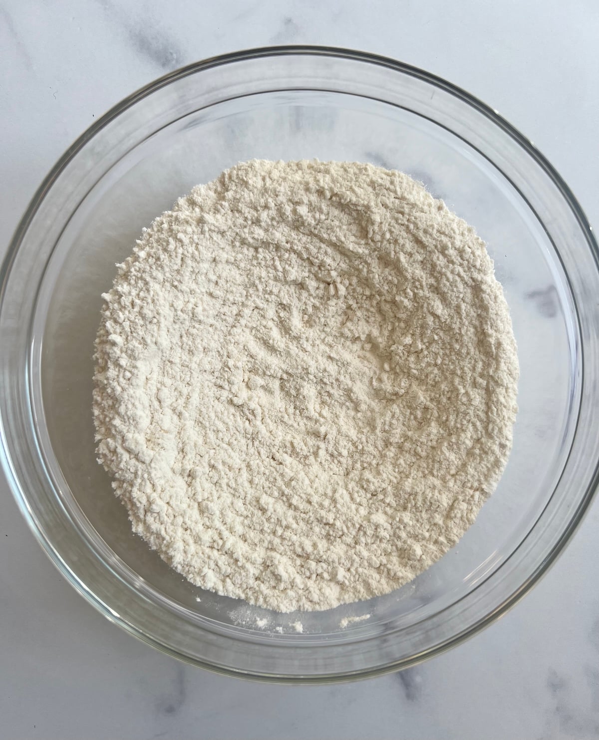 Dry ingredients for strawberry muffins whisked together in a glass mixing bowl on a marble surface