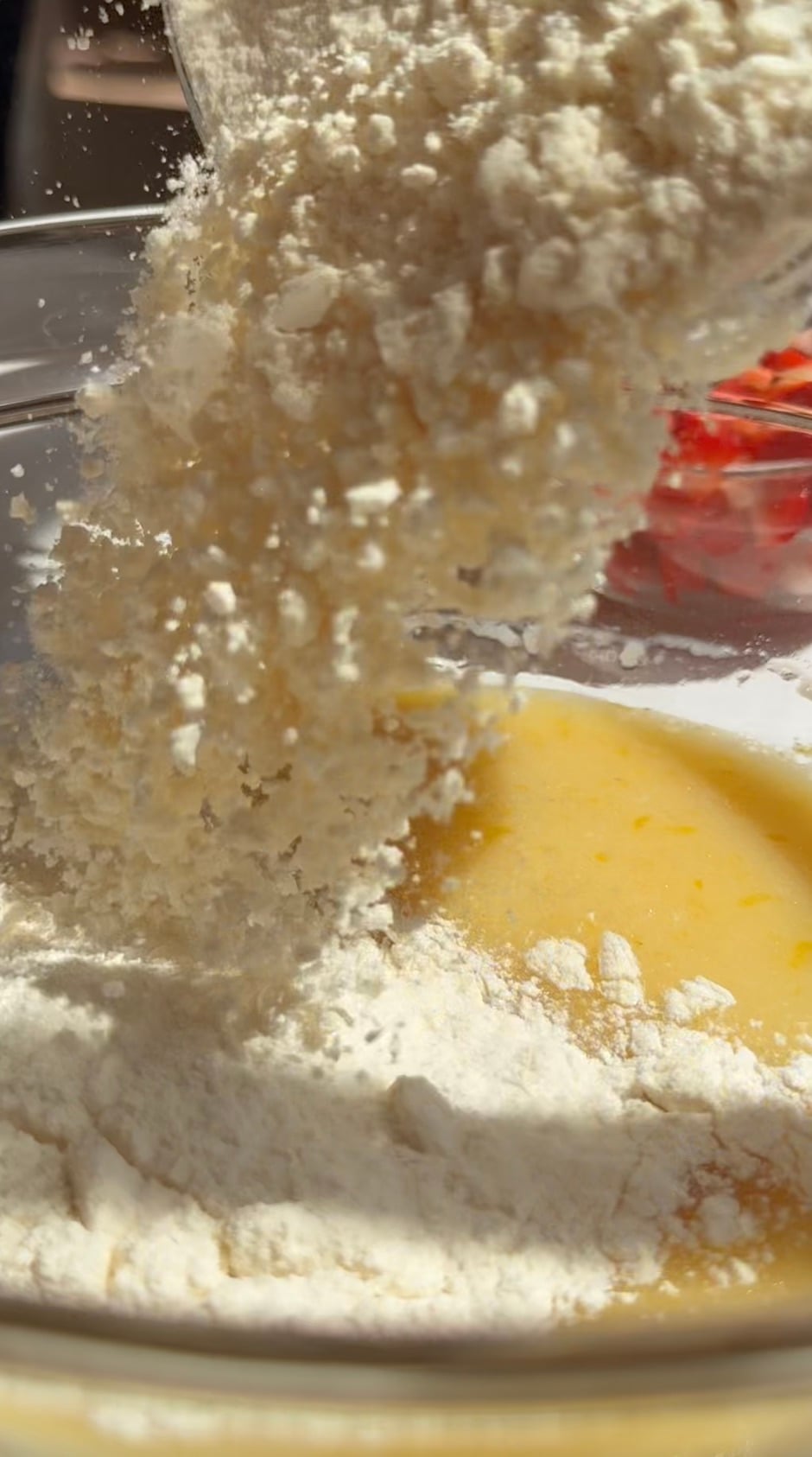 Dry ingredients being poured into wet ingredients in a glass bowl to make strawberry muffin batter.