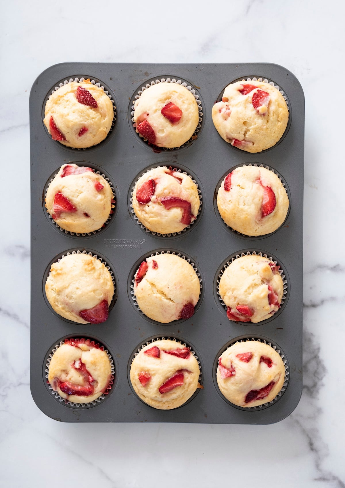 A pan of freshly baked strawberry muffins golden and risen.