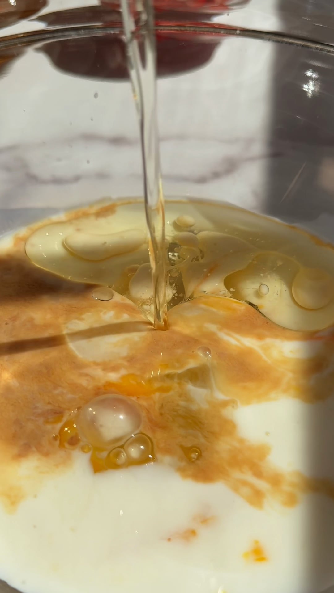 Honey being poured into milk and oil in a glass bowl to make strawberry muffin batter.
