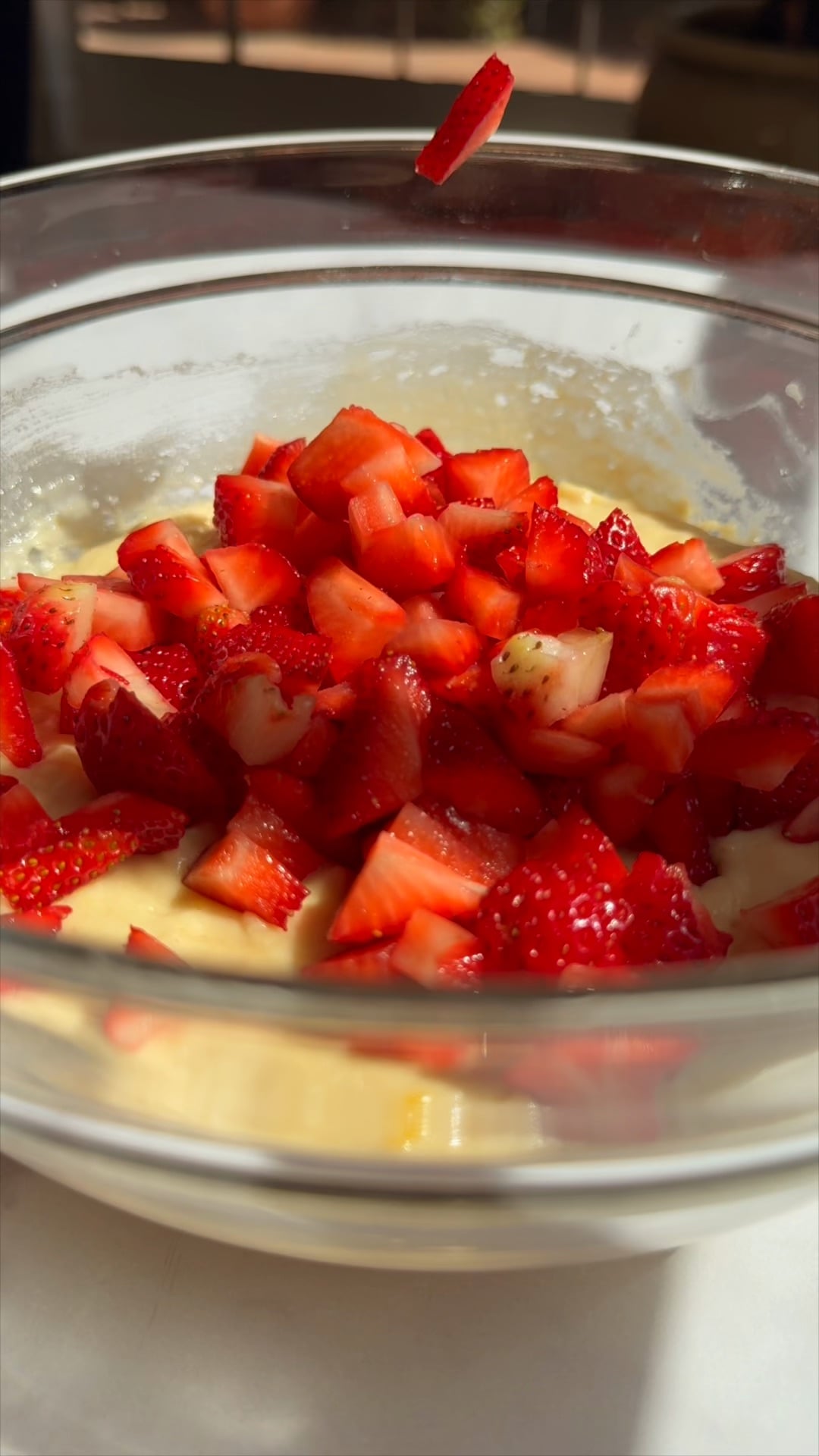 Fresh diced strawberries being added to strawberry muffin batter in a glass bowl.