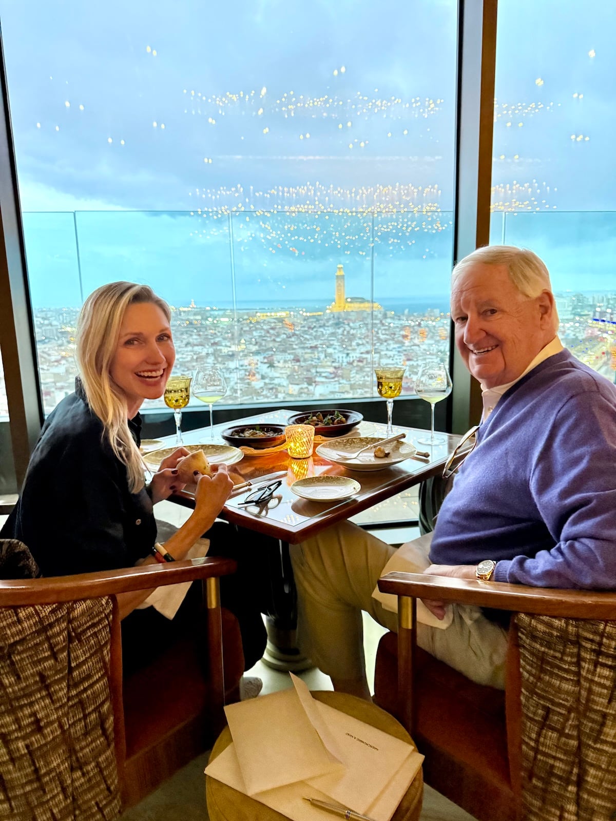 Catherine and her dad dining at La Grande Table Marocaine, with the Hassan II Mosque lit up against the Casablanca skyline through the floor-to-ceiling windows.