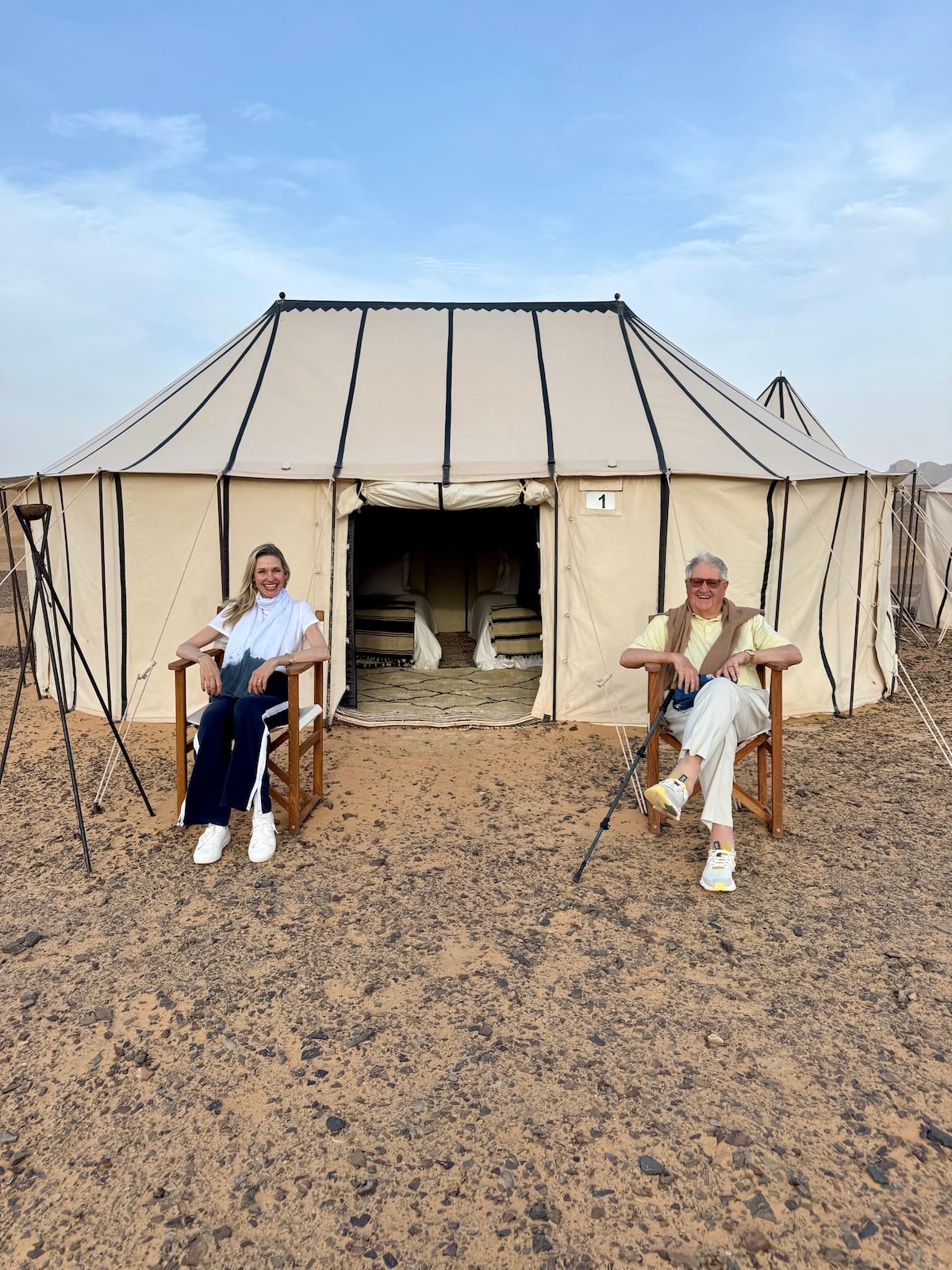 Catherine and her dad sitting outside their desert camp tent, Sahara dunes in the background.