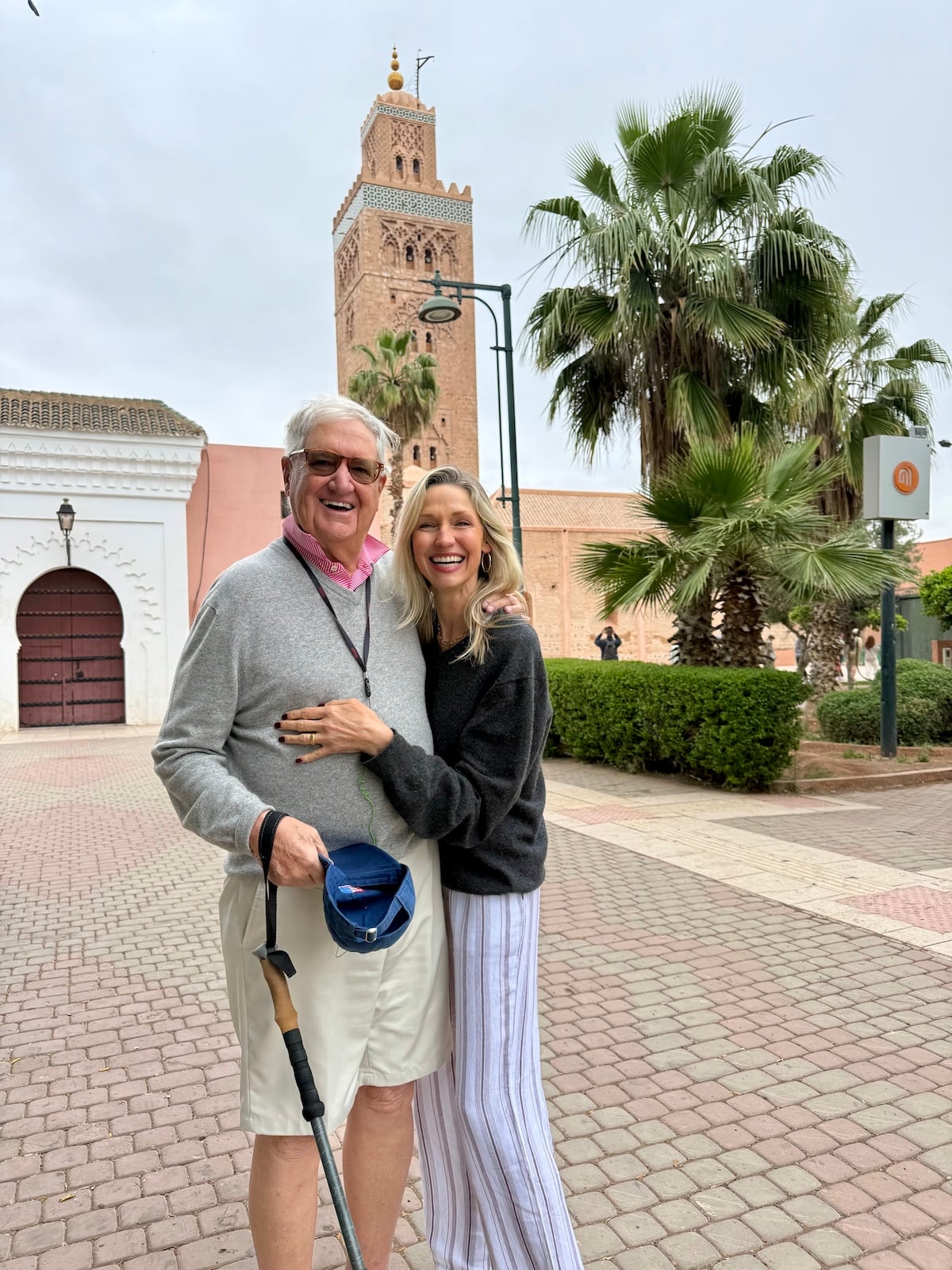 Catherine and her dad walking near the Koutoubia Mosque in Marrakech, palm trees and blue sky behind them.