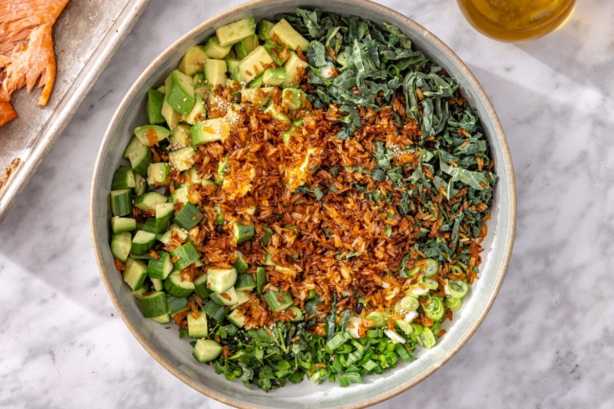 Golden crispy chili crisp rice added to salad bowl with kale, avocado, and cucumber.