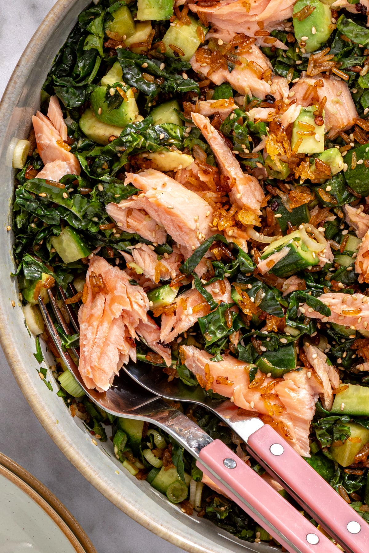 Overhead view of crispy rice salmon salad with flaked salmon, avocado, and kale in a ceramic bowl.