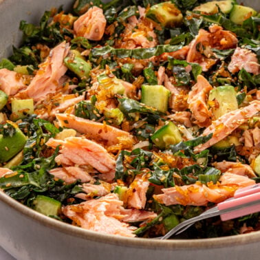 Crispy rice salmon salad with flaked salmon, avocado, and kale in a ceramic bowl.