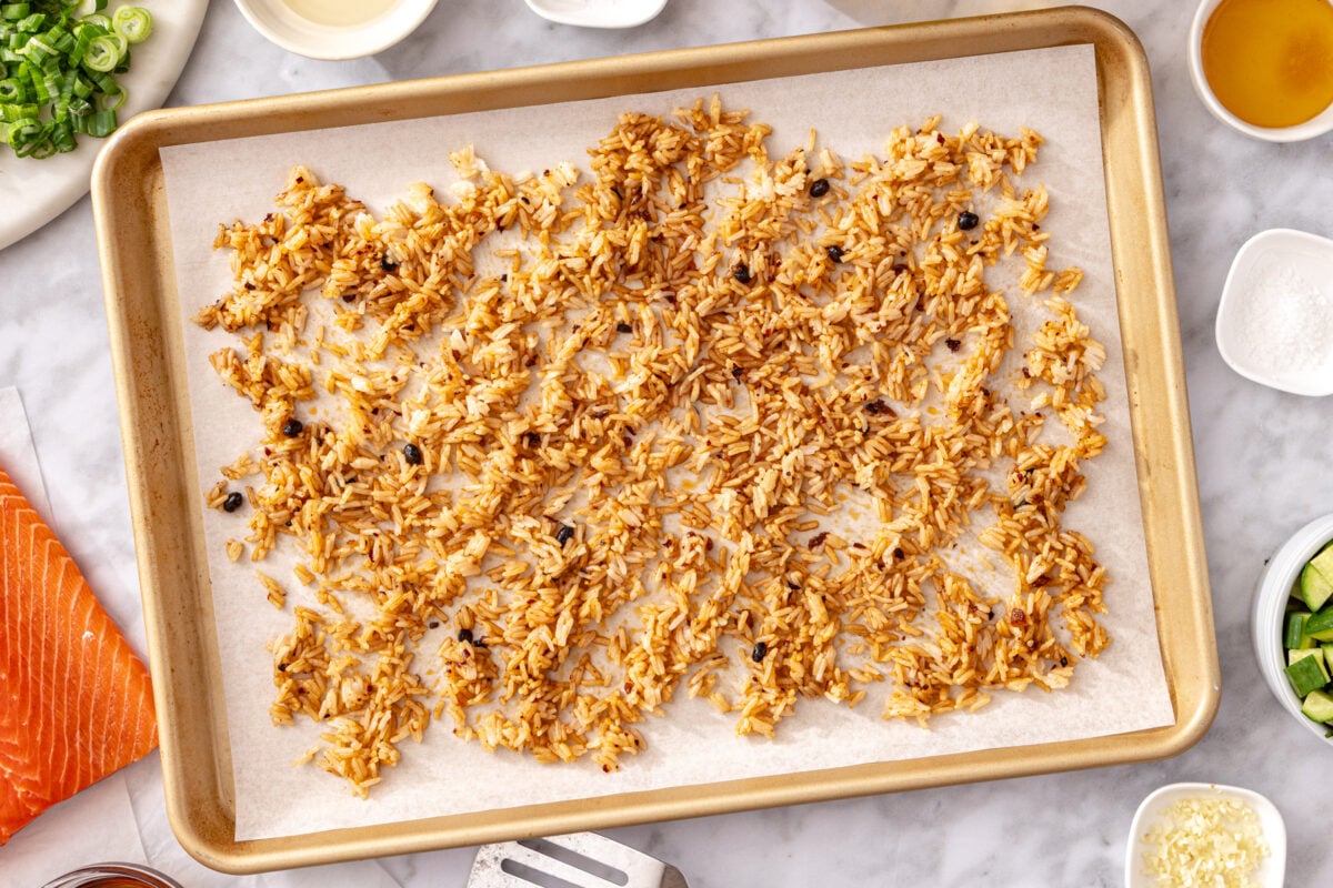 Chili crisp seasoned jasmine rice spread on a parchment lined sheet pan ready to bake.
