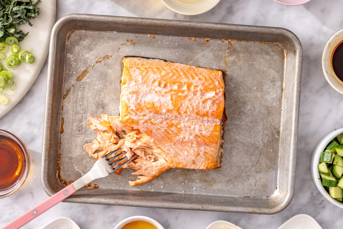Broiled salmon fillet being flaked with a fork on a sheet pan for crispy rice salmon salad.