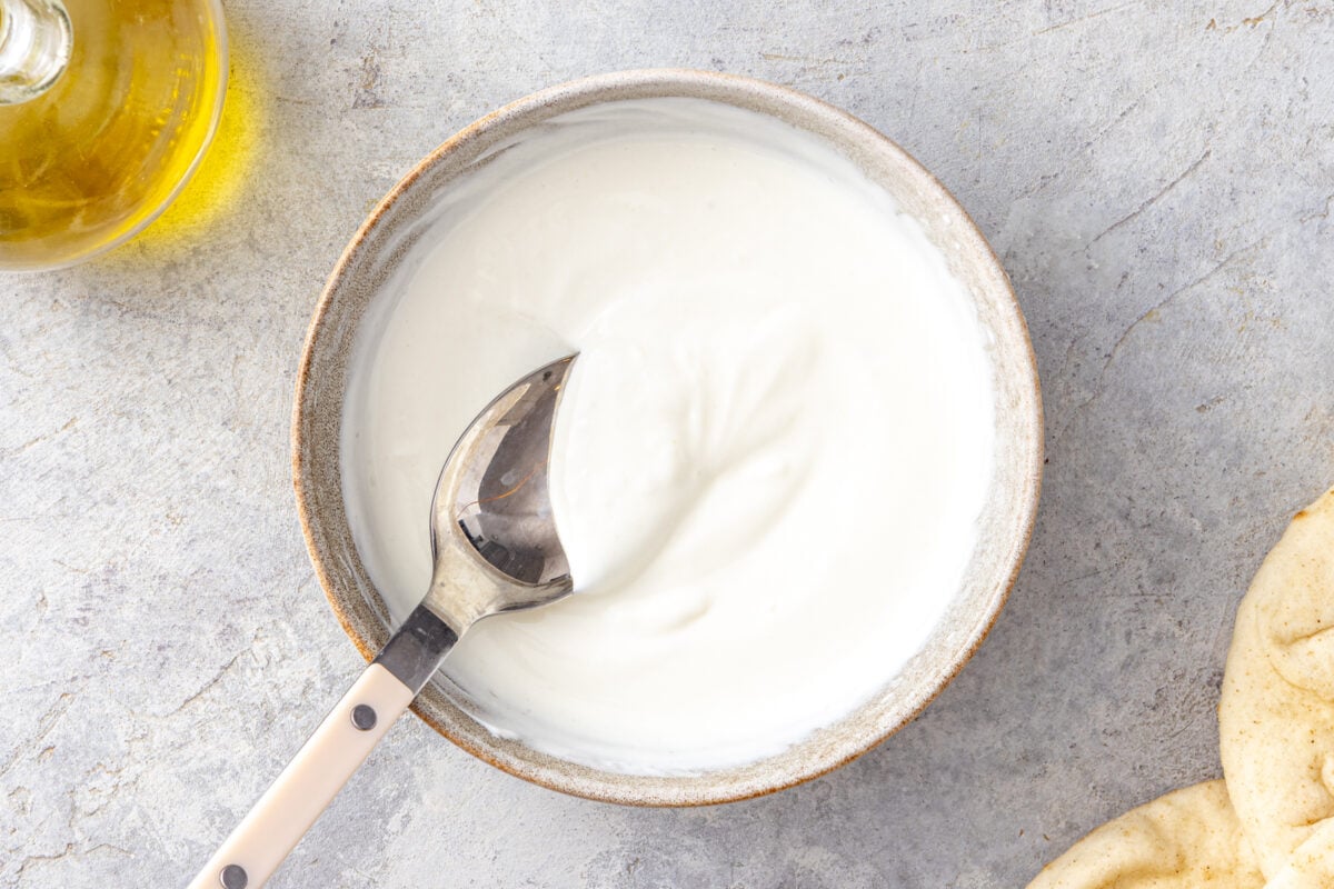 Creamy lemony yogurt sauce whisked together in a ceramic bowl for homemade doner kebab.