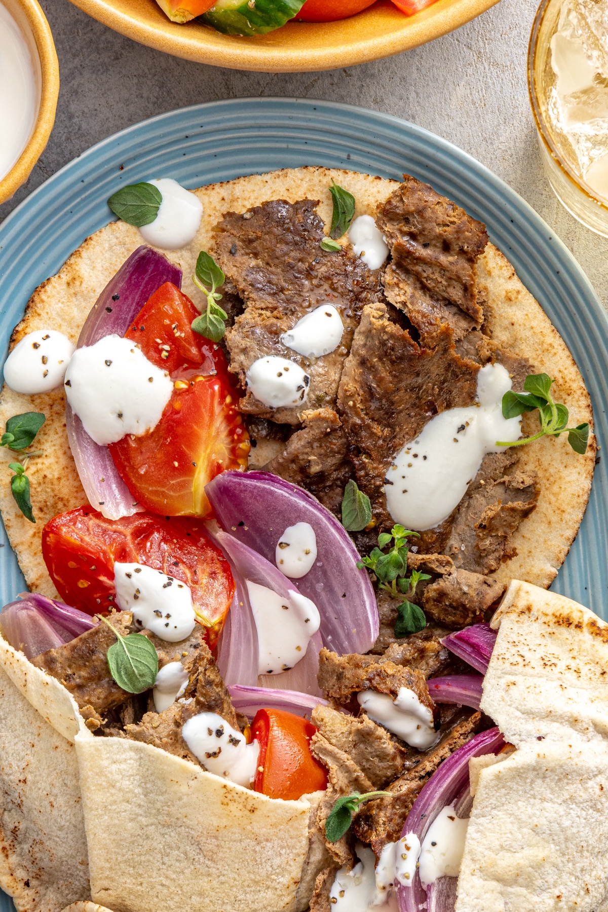 Close up of homemade doner kebab on open faced pita with crispy spiced meat, roasted tomatoes, red onion, and yogurt sauce.