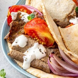 Homemade doner kebab stuffed inside warm pita pockets with roasted tomatoes, red onion, and yogurt sauce on a blue platter.